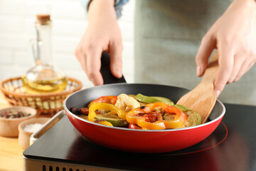 Woman frying vegetables in pan on stove at table indoors, closeup
