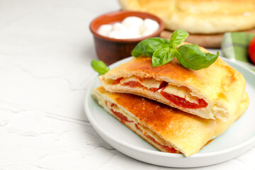 Pieces of tasty vegetarian calzone with tomato, cheese and basil on white textured table, closeup. Space for text