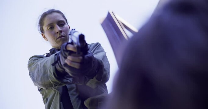 Grim female solider pulling out pistol and executing person on the ground
