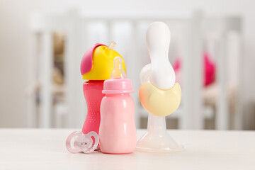 Feeding bottles with milk, breast pump and pacifier on white table indoors