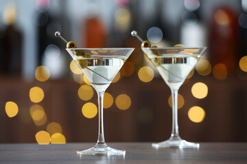 Martini cocktail with olives in glasses on wooden table against blurred background. Bokeh effect
