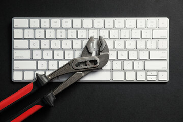 Technical support concept. Plumbing pliers and keyboard on black background, top view