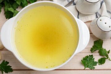 Tasty chicken bouillon in bowl and ingredients on wooden table, flat lay