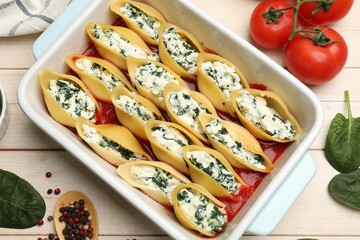 Delicious pasta with ricotta cheese, spinach and tomato sauce in baking dish on wooden table, flat...