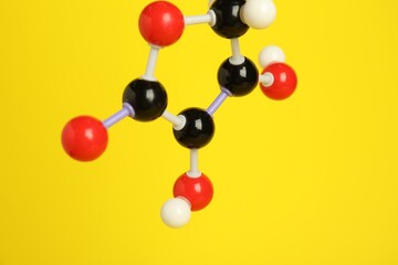 Molecule of vitamin C on yellow background, closeup. Chemical model