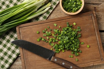 Fresh green onions and knife on wooden table, flat lay