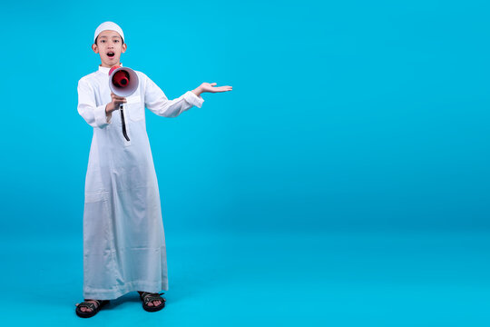 Full Body Shot Of Young Asian Muslim Boy Announce Using Megaphone While Presenting Isolated On Blue Background