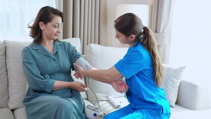 Caregiver caucasian young nurse woman measuring blood pressure with patient for checkup pulse health and examining in living room at home, nurse checkup patient for health care, medical and insurance.