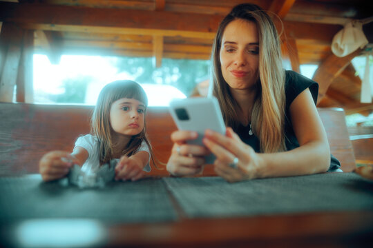 Little Girl Looking at the Smartphone of her Mom in a Restaurant. Mother overusing technology ignoring her little one
- Powered by Adobe