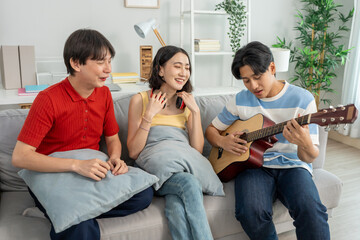 Diverse Asian friends playing guitar and dancing in living room at home. 