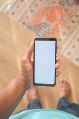 Hand holding a blank smartphone in a cozy indoor setting