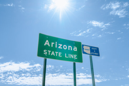 Horizontal image of Arizona State Line with adopt a highway sign adjacent to it.