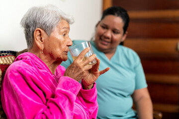 Nurse assisting elderly woman drinking water at home