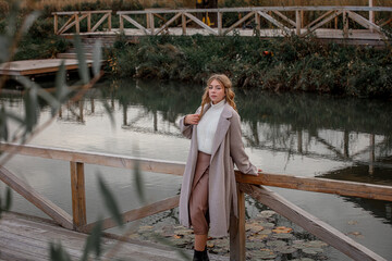A blonde model girl walks along the pier against the background of the lake