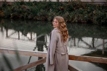 A blonde model girl walks along the pier against the background of the lake