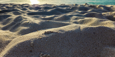 low angle view of rolling mounds of beach sand caused by passing feet. sunset with aquamarine ocean in background and bokeh lighting effect.