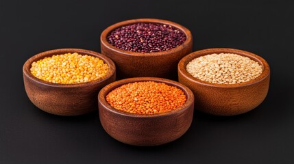 Four wooden bowls filled with different types of lentils and quinoa on a black background. Healthy eating concept.