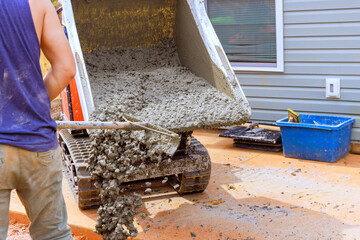 Construction worker uses shovel to pour wet concrete from concrete buggy for patio