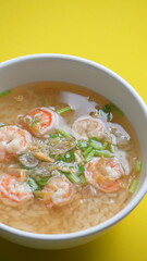 rice soup with shrimp in white bowl on yellow background