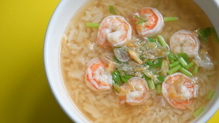 rice soup with shrimp in white bowl on yellow background