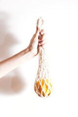 Person holding a rope bag with an orange inside against a white background