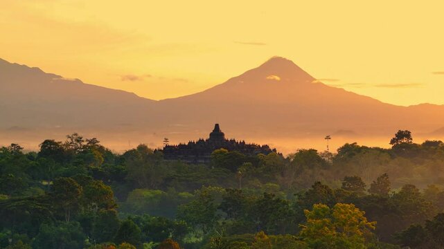 Aerial drone view of temple emerge among green trees and silhouette mountain background in sunrise, Borobudur, Central Java, Indonesia.