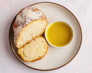 A freshly baked loaf of bread on a plate, sliced in half, served with a small bowl of golden olive oil for dipping.