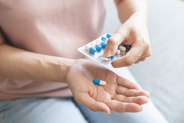 Sick ill asian young woman, girl hand taking tablet pill capsule out from blister pack, painkiller medicine from stomach pain, head ache, pain for treatment, take drug or vitamin at home, health care.