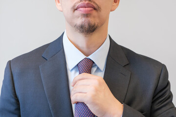 A man in a business suit corrects a tie on the shirt close-up on gray background, front view.