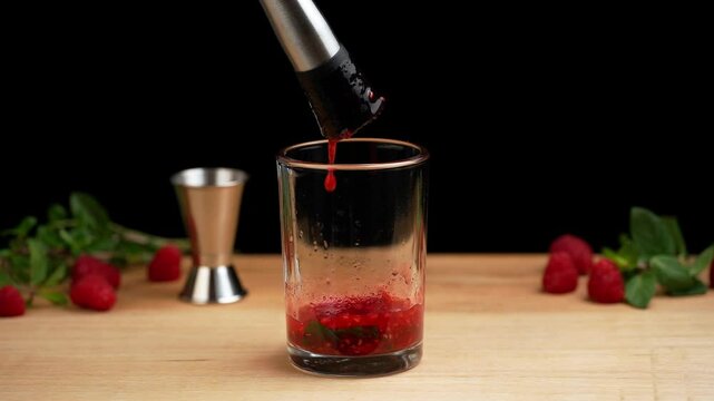 Preparing a raspberry mojito, mashing raspberries and mint leaves with a muddler to prepare a mojito
