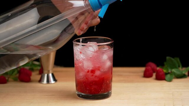 Preparing a raspberry mojito, pouring mineral water into a mojito cocktail