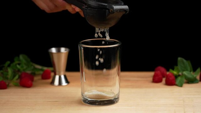 Preparing a raspberry mojito, squeezing lime juice with a juicer to prepare a mojito, black background, slow motion