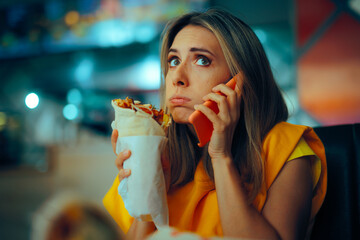 Stressed Woman Talking on the Phone and Eating in Shawarma Restaurant. Lady multitasking...