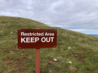 Restricted Area KEEP OUT warning sign stands on a grassy hillside under an overcast sky
