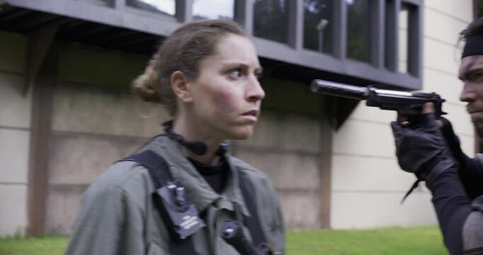 Female soldier looking around suspiciously then turning back around to see man pointing silencer at face, screaming 