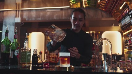 Asian bartender pouring mixed cocktail whiskey into cool glass textured cooling ice drink making special advertisement creative focusing alcohol refresh showcase at luxurious warm light pub. Vinosity.