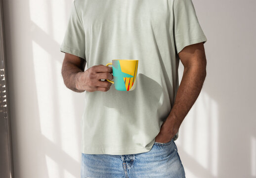 Handmade ceramic mug with handle held by man in a casual setting with soft light. PSD template mockup