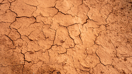 Close-up of parched, cracked earth with deep fissures and a rough, textured surface. The warm, reddish-brown tones highlight drought, arid landscapes, and climate change effects on dry, barren soil.