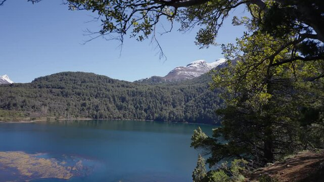A scenic beauty of a river named Arrayanes located in Parque Nacional Los Alerces, we can find the blue sky with a mountain in the background