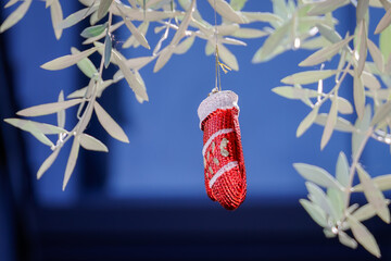 A close-up of a red mitten-shaped Christmas ornament with golden accents and white trim