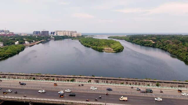 Aerial side view of vehicles apssing over bridge with small green lush island at background.