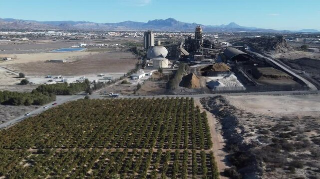 Flying away from a huge cement factory and over a citrus plantation. San Vicente del Raspeig, Spain.