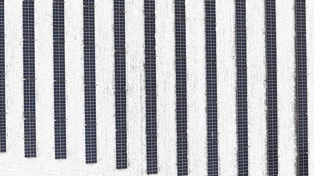 Solar panels covered in snow, arranged in parallel rows, captured from an aerial view