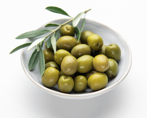 Green olives with olive branch resting in a bowl on white background