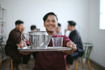 Portrait of Muslim Man Holding a Tray With Pitcher and Glass During Iftar With Friends