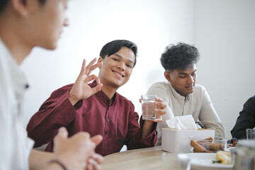 Muslim Young Man Showing Okay Sign While Holding a Glass of Water to Breaking Fast Together in The Dining Room