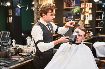 Experienced hairdresser styling client's hair. Handsome hairstylist in fancy outfit at work. Male barber using professional hairdryer and brush.