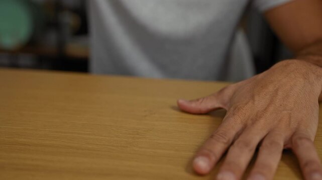 Young man holding a blue cup indoors at a wooden table in an office setting focusing on hands and simple room details.