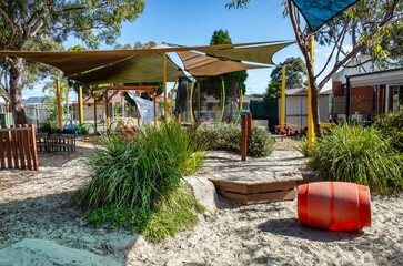 An outdoor play area at a kindergarten or childcare center featuring natural elements including...