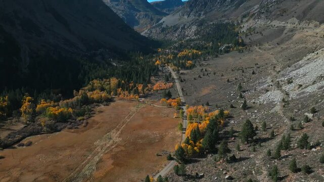 West Portal Entrance rugged Mountains Lee Vining Tioga Pass Road Yosemite National Park aerial drone California Ansel Adams Wilderness autumn fall yellow orange Aspen Trees blue sky forward pan up